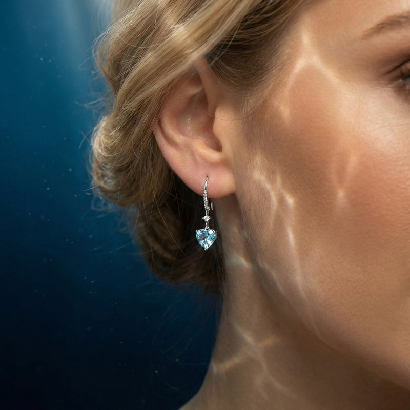 Heart cut aquamarine and platinum drop earring with diamond accents worn on a woman's ear.