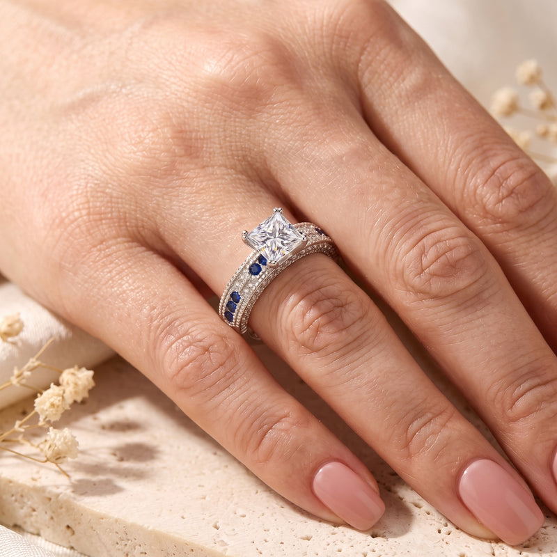 Princess-cut silver ring with blue sapphire accents worn on a woman's finger.