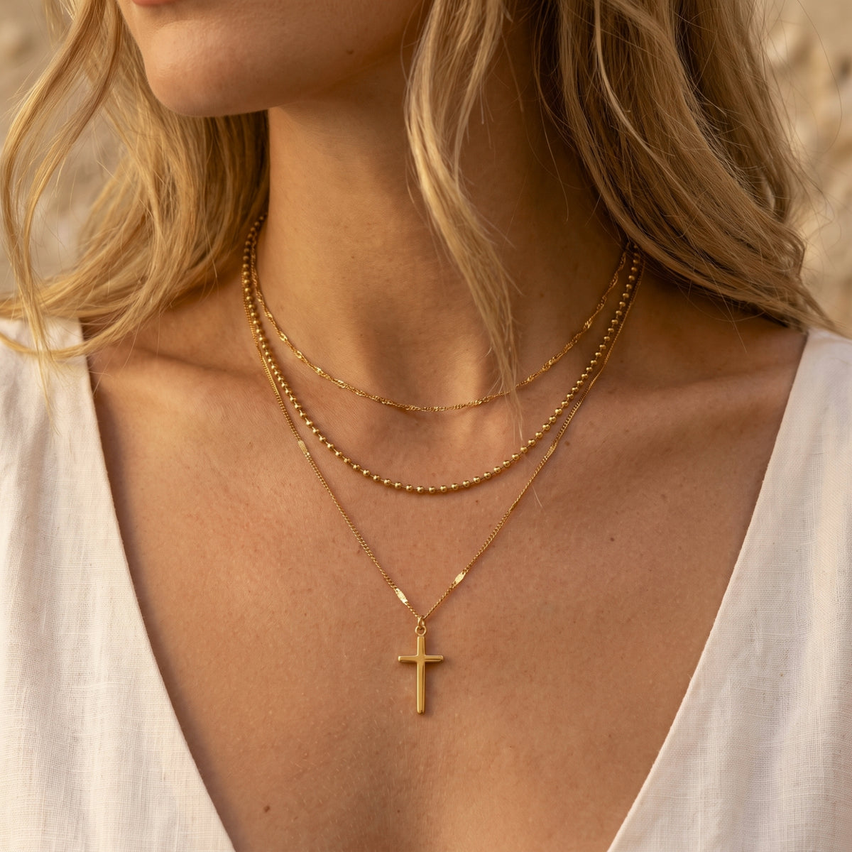 Close-up of a woman wearing a gold-tone layered necklace with a cross pendant and varied chain textures.