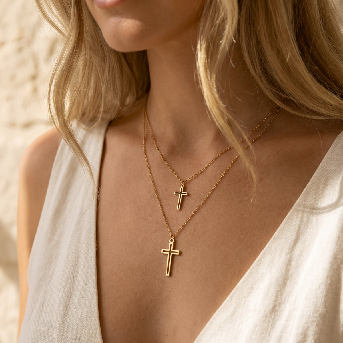 Angled close-up of a person wearing the layered gold-tone double cross necklace over a white sleeveless top.