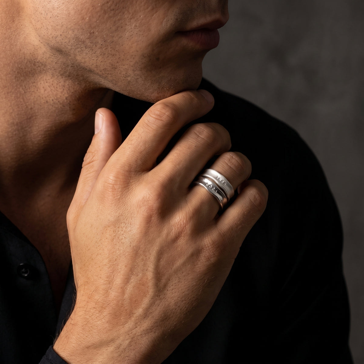 Man wearing two stacked textured silver open-band rings on his ring finger while resting his hand near his chin