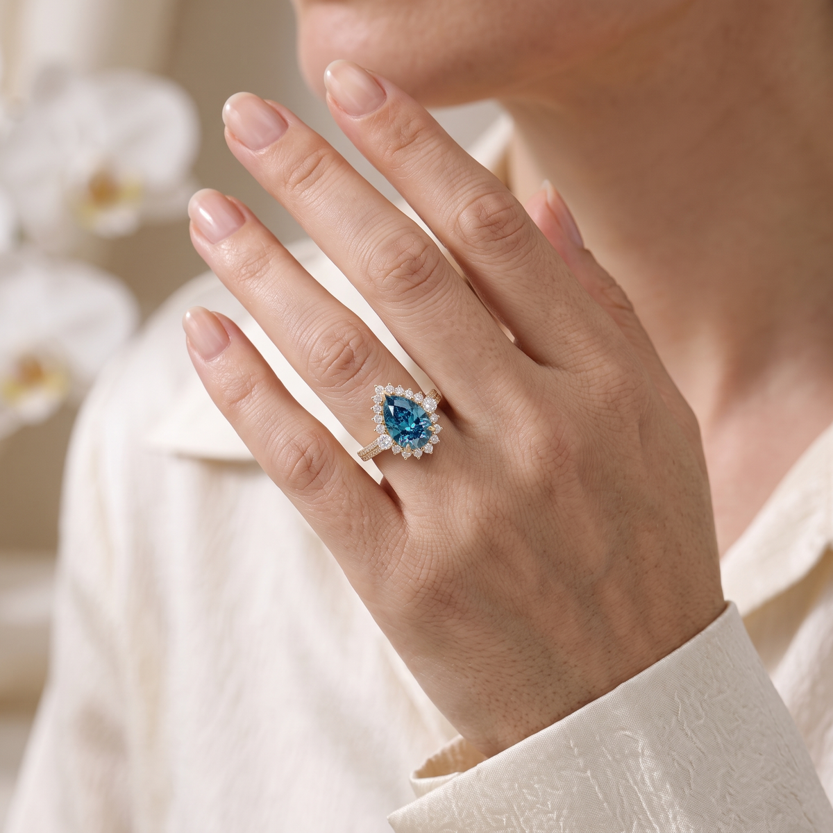 Model wearing a pear cut blue moissanite halo ring in rose gold on her ring finger.