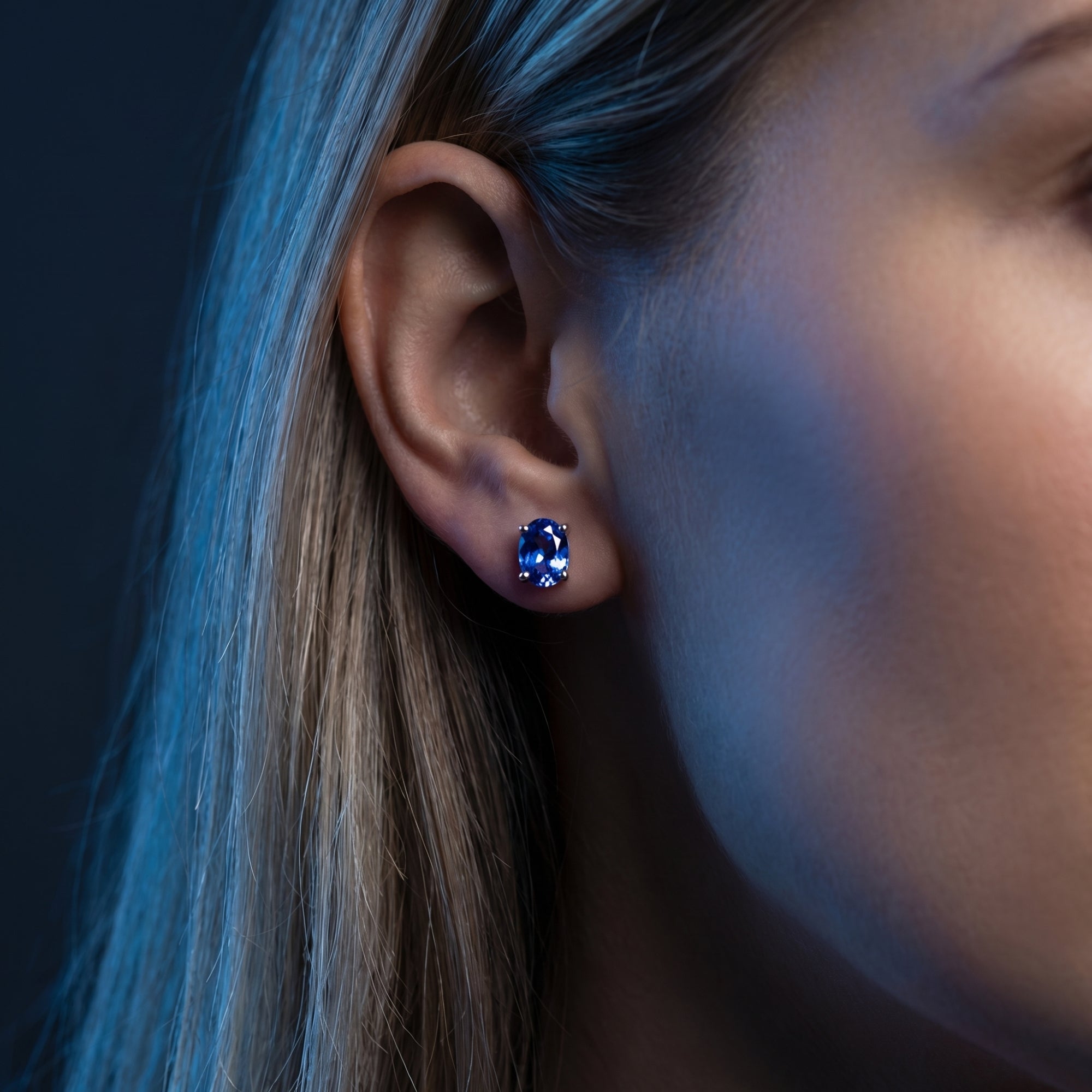 Woman wearing an 18K white gold oval cut natural tanzanite stud earring.