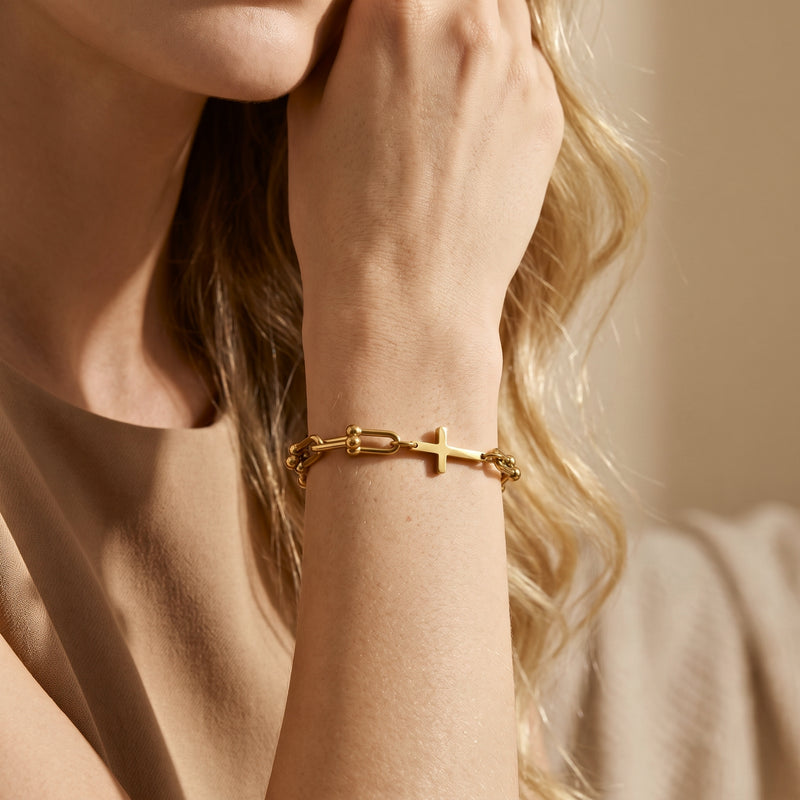 Close-up of a gold-tone U-link cross bracelet worn on a wrist against a neutral beige top.