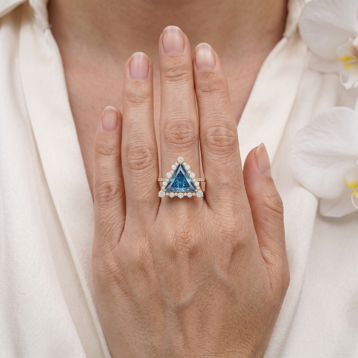 Close-up of a woman's hand wearing a trillion cut blue moissanite halo ring in rose gold.