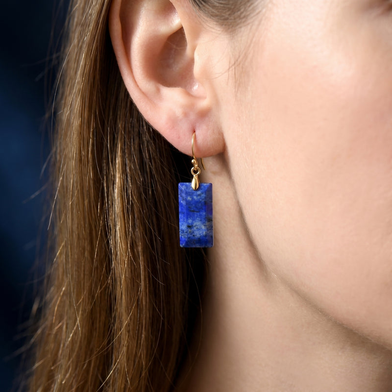 Close-up of a model wearing a rectangular natural lapis lazuli drop earring with a gold hook.