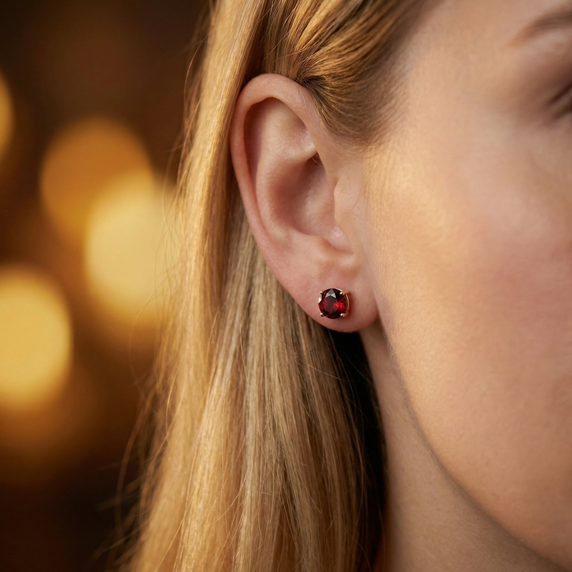 Aethelis 18K white gold stud earring with a round-cut red garnet shown worn on a woman's ear.