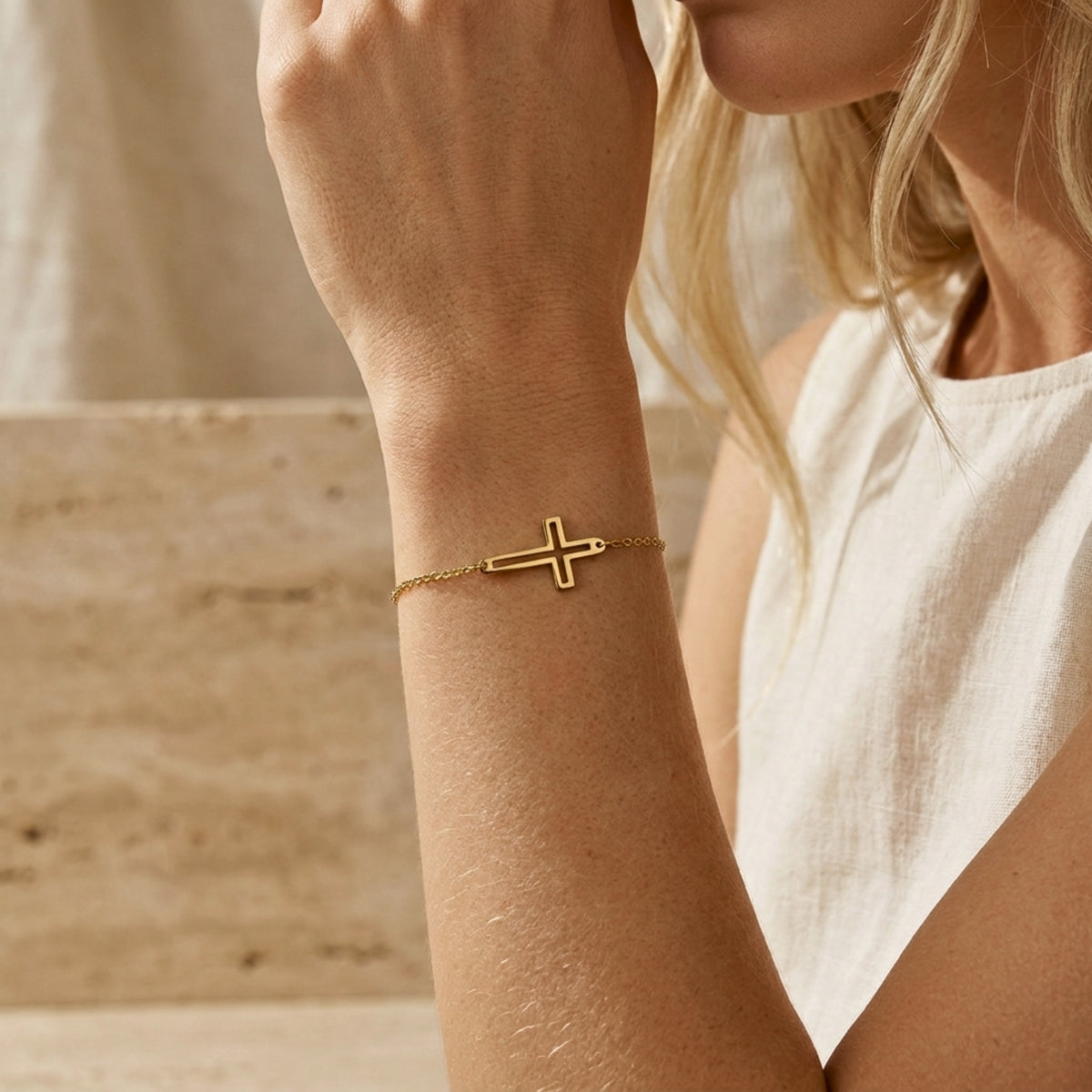 Model wearing the gold-tone cutout cross chain bracelet on her wrist with a white sleeveless top.