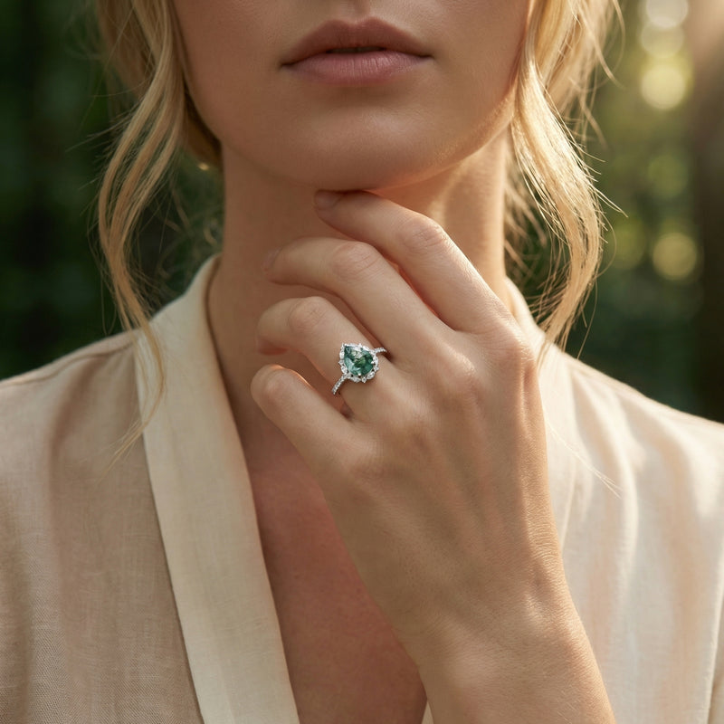 Model wearing a pear cut moss agate halo ring in sterling silver on her finger, paired with a neutral linen outfit.
