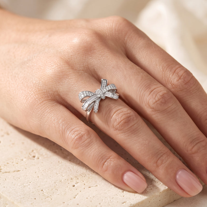 Sterling silver baguette bow promise ring worn on a woman's hand.