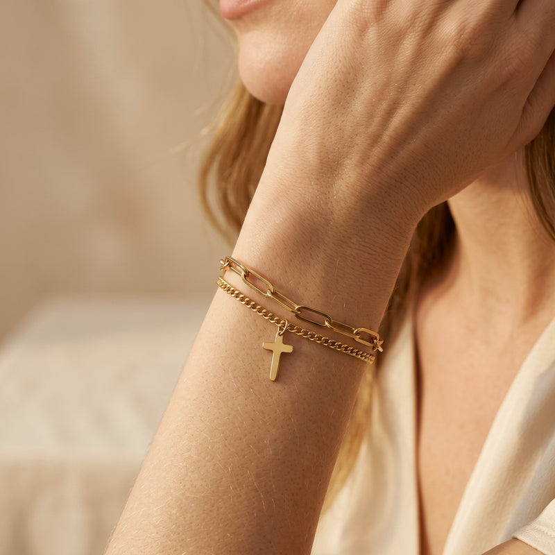 Close-up of the gold-tone layered cross bracelet worn on a wrist, showing its two chain styles.