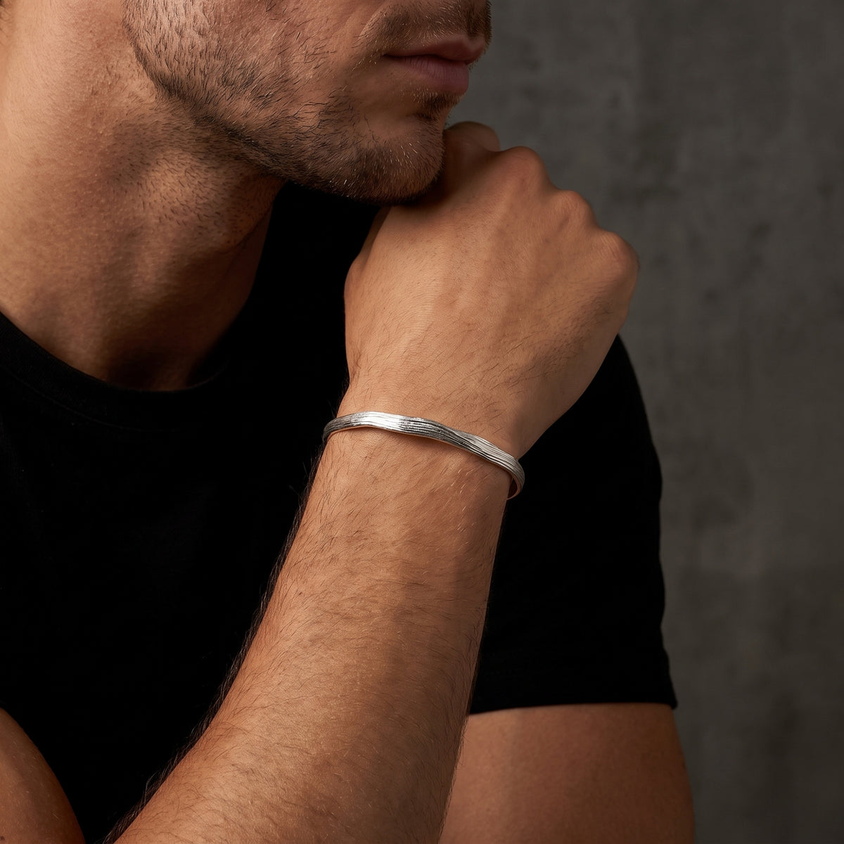 Man wearing a textured silver open cuff bracelet on his wrist against a black shirt.