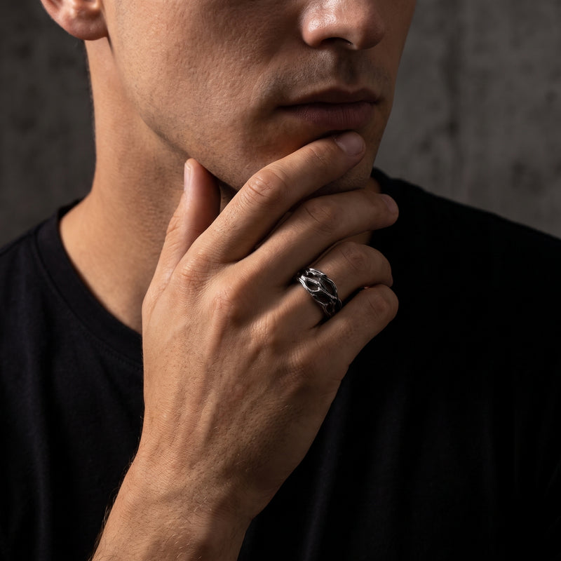 Model wearing the textured openwork silver ring on his ring finger while resting his hand at his chin.