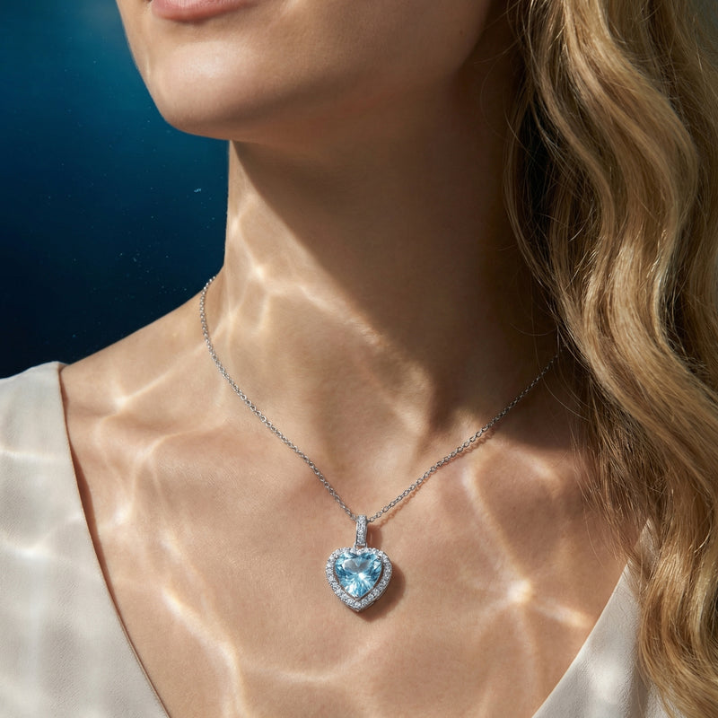 Woman wearing the heart-cut natural aquamarine halo pendant in platinum with shimmering light reflections on her skin.
