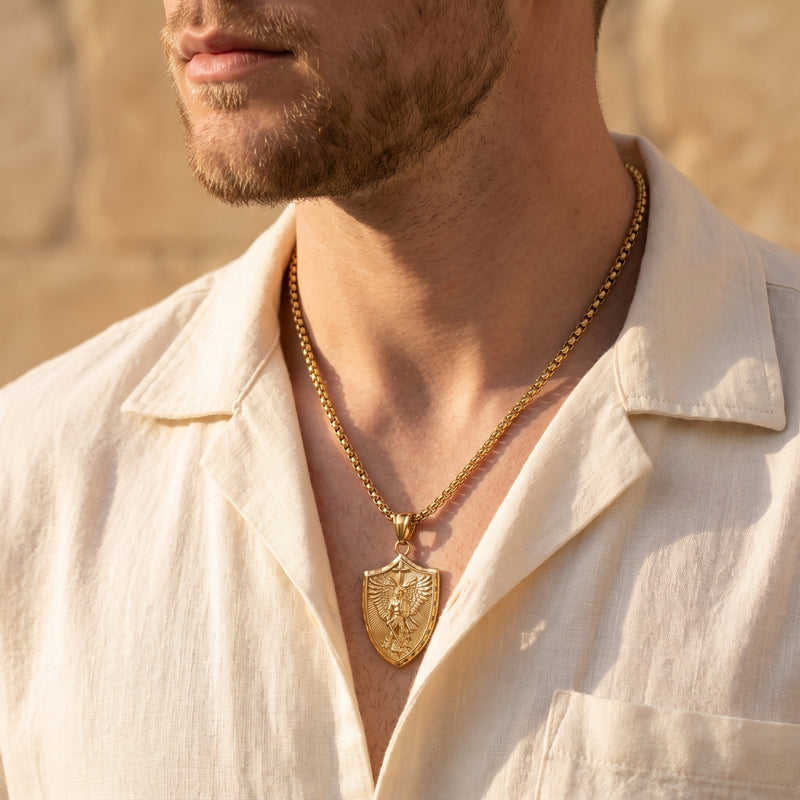 Close-up of a man wearing the gold-tone archangel shield pendant necklace with a box chain and open collar.