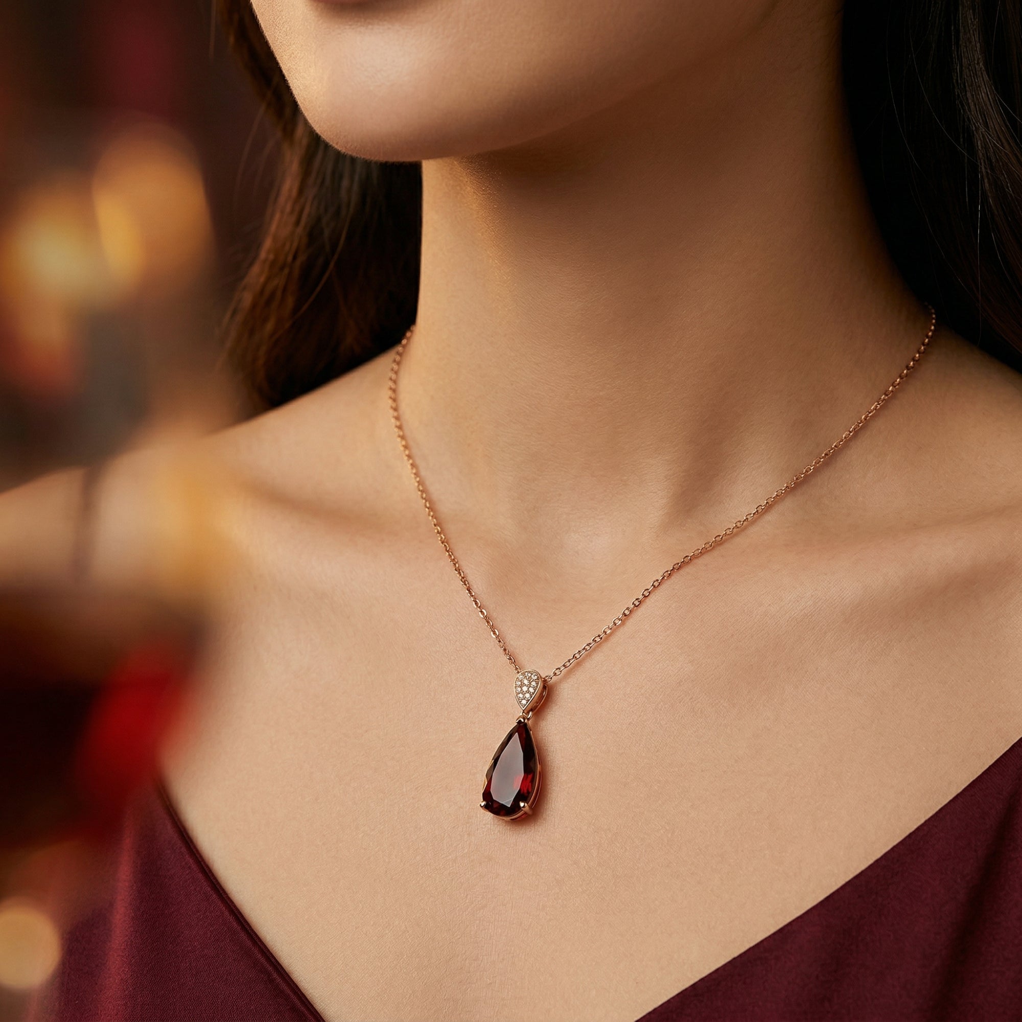 Model wearing the Calista pear-cut natural garnet necklace in 18K rose gold against a dark red dress.