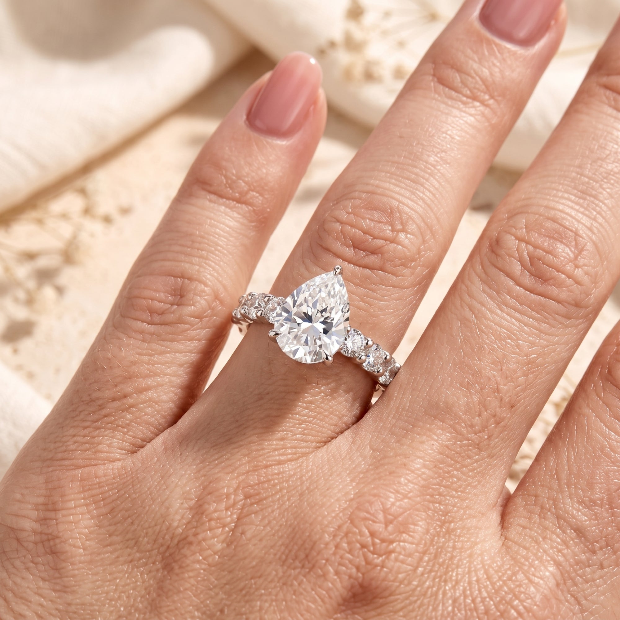 Pear-cut silver promise ring worn on a finger showing stone brilliance.