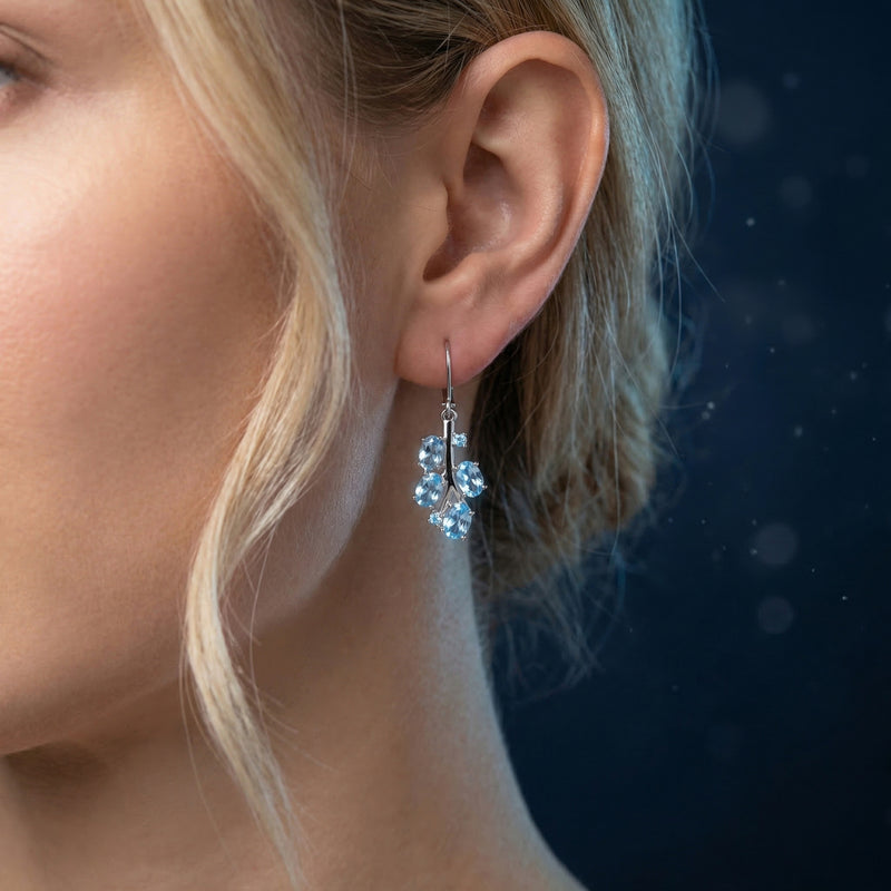 Model wearing a silver drop earring featuring a cluster of oval and round Swiss blue topaz gemstones.