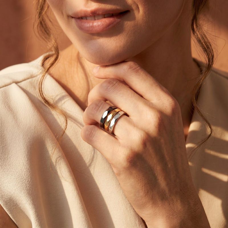 Model wearing a stack of three faceted Keira rings in black, gold, and silver stainless steel.
