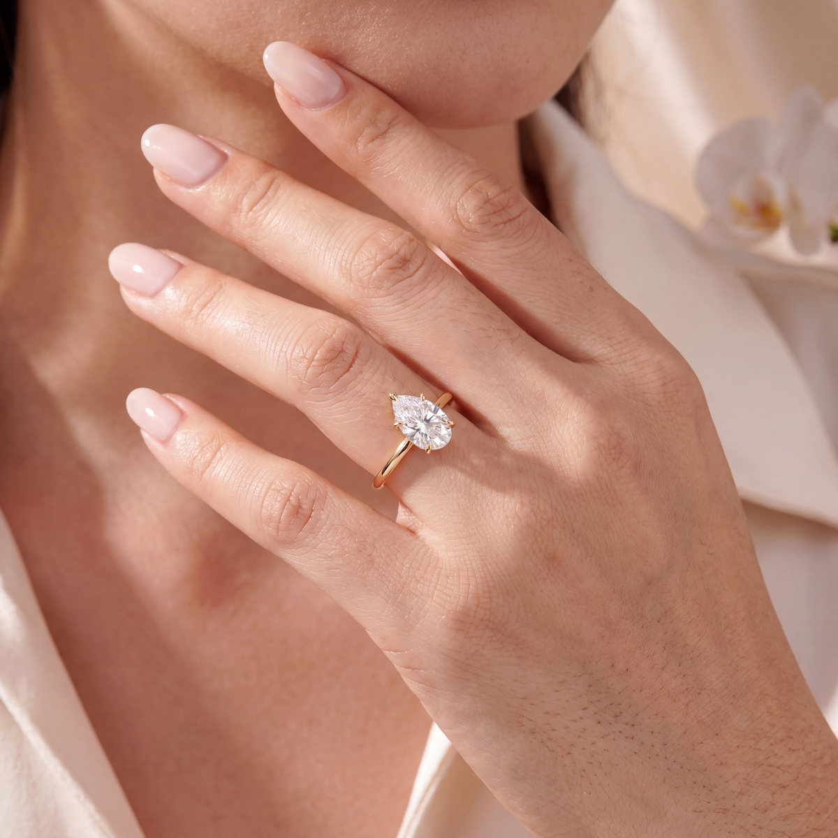 A pear-cut moissanite solitaire ring in yellow gold worn on a hand.