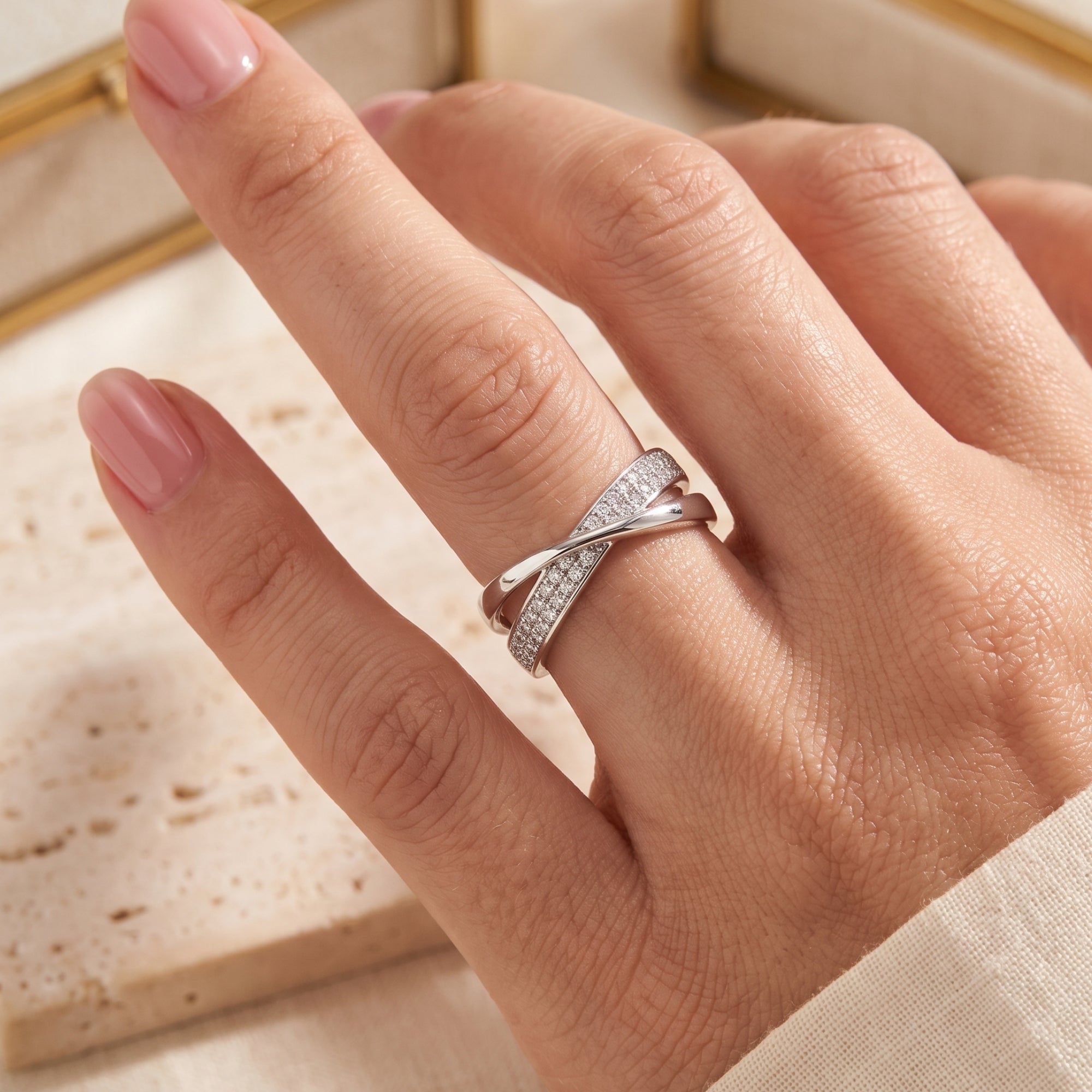 Silver intertwined crossover ring with pavé stones worn on a finger.
