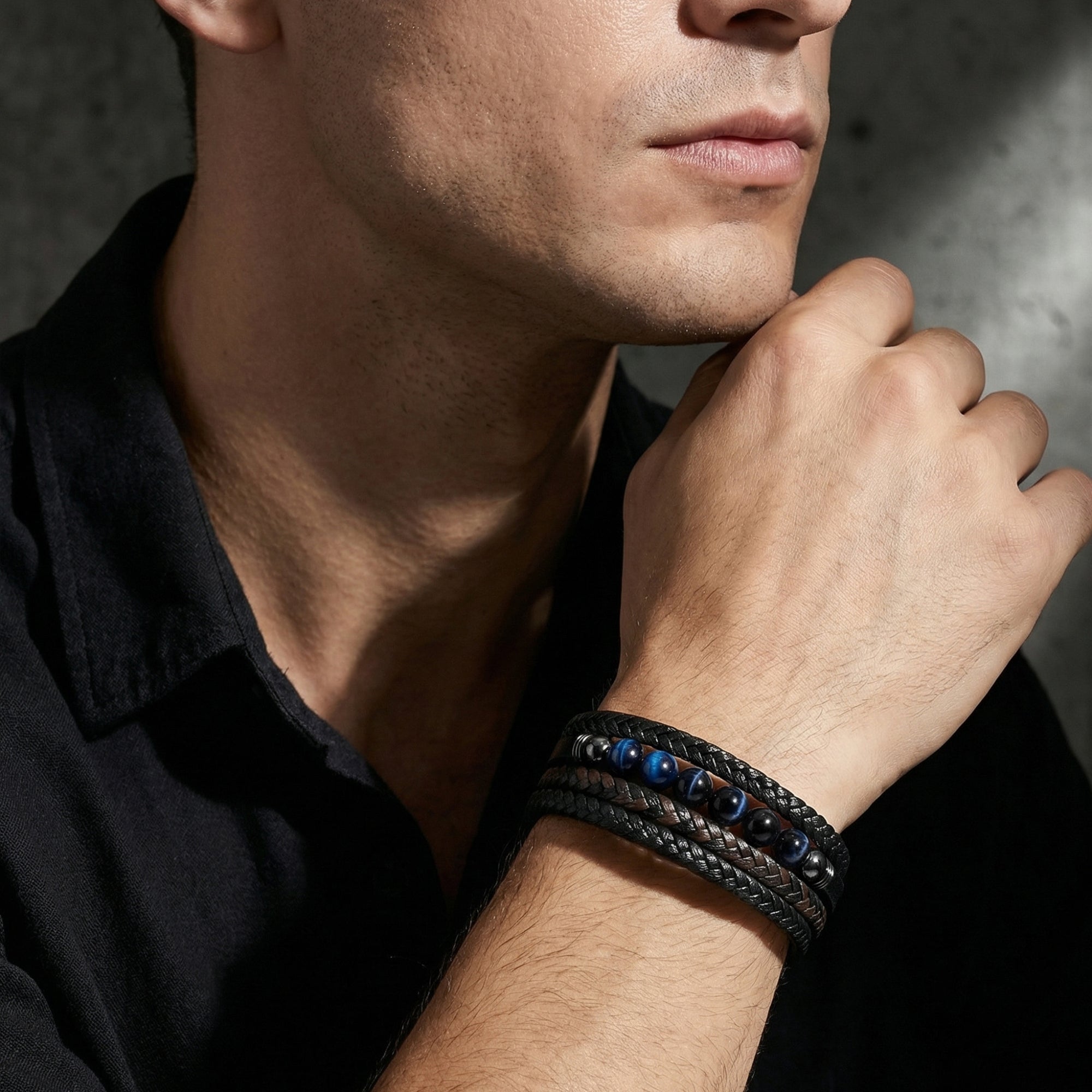 Men's multi-layered black leather bracelet with blue beads worn on a wrist, styled with a black button-down shirt.