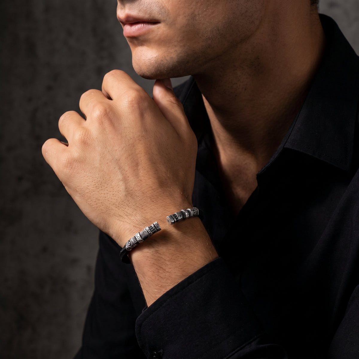 Man wearing the carved silver open cuff bracelet on his wrist while touching his chin.