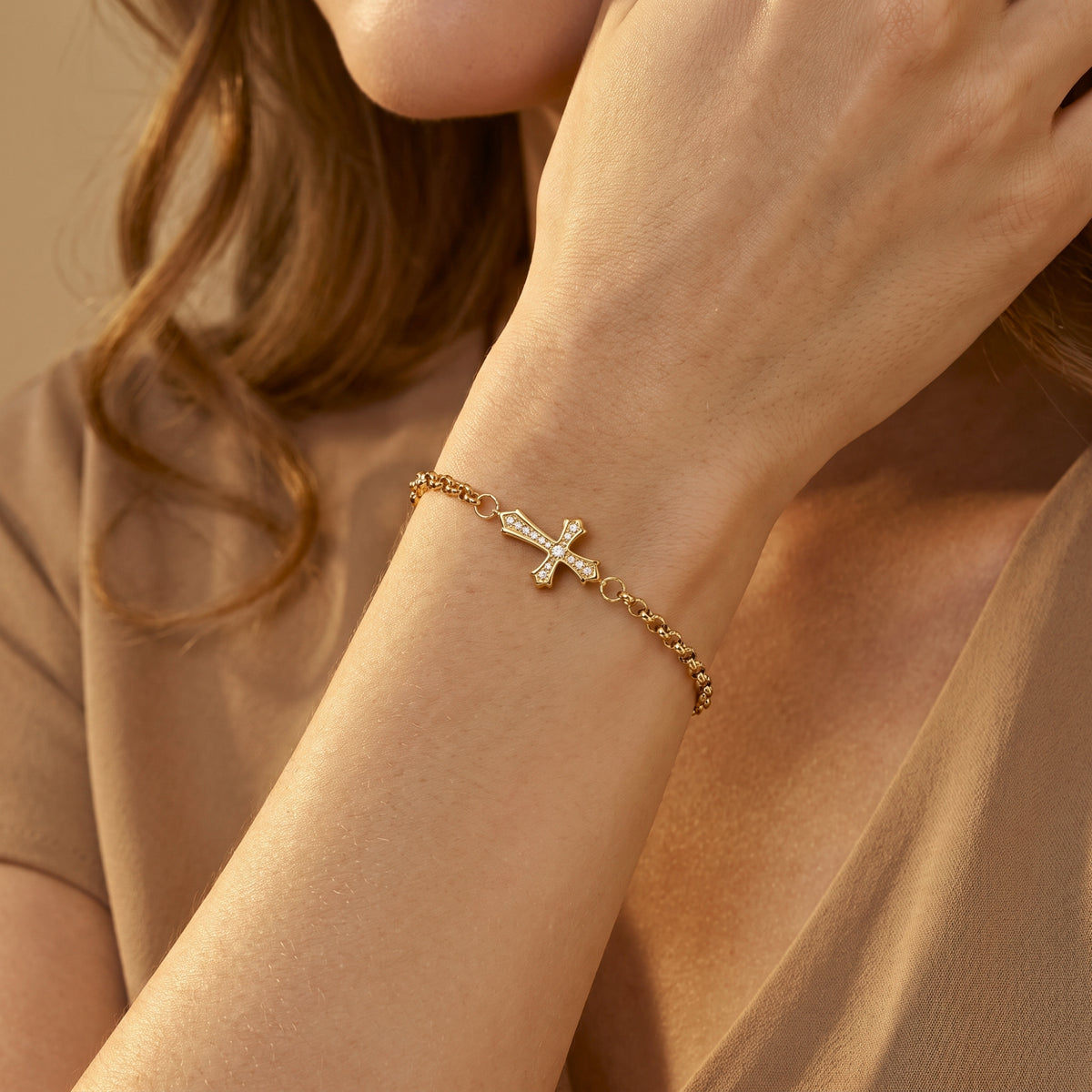 Close-up of a wrist wearing a gold-tone cross bracelet with sparkling stones.