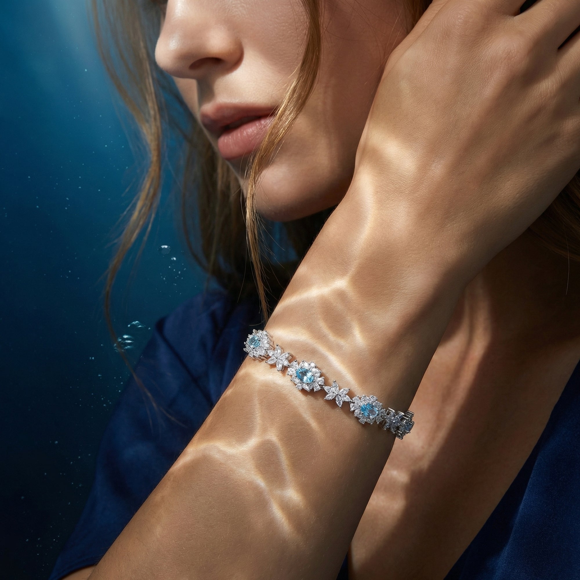 Women's silver aquamarine station bracelet worn on a wrist with shimmering water light reflections.