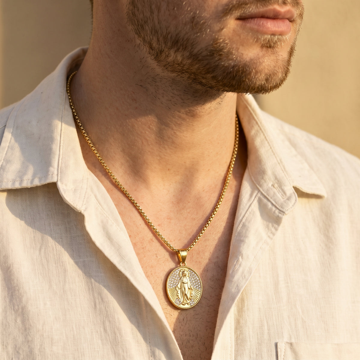 Man wearing a gold-tone oval Miraculous Medal necklace centered over an open white shirt.