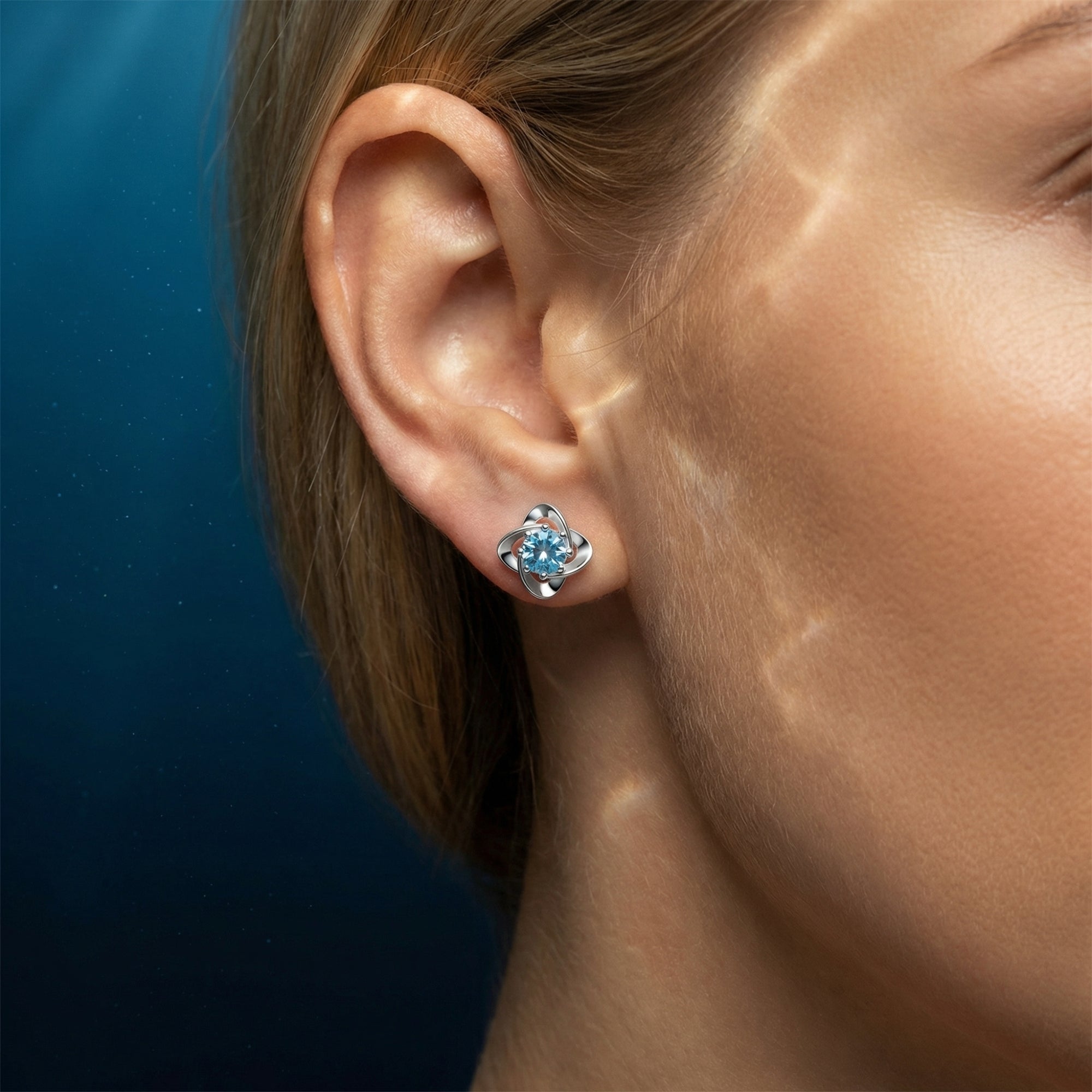 A round cut aquamarine stud earring in platinum worn on a woman's ear with watery light reflections.