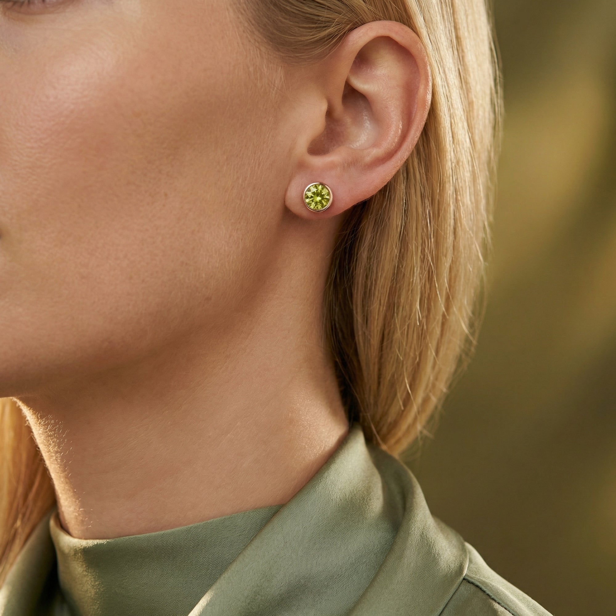 A woman wearing a round cut peridot stud earring in 18K rose gold vermeil, styled with a green silk blouse.