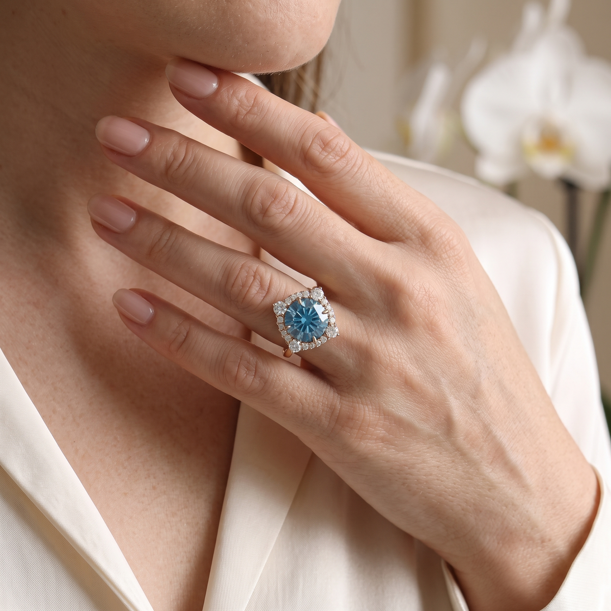 Rose gold blue round moissanite halo engagement ring worn on a woman's finger.