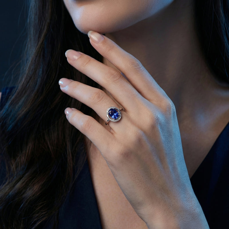 Woman wearing the Seraphiel oval tanzanite ring in 18K white gold with a diamond halo on her ring finger.