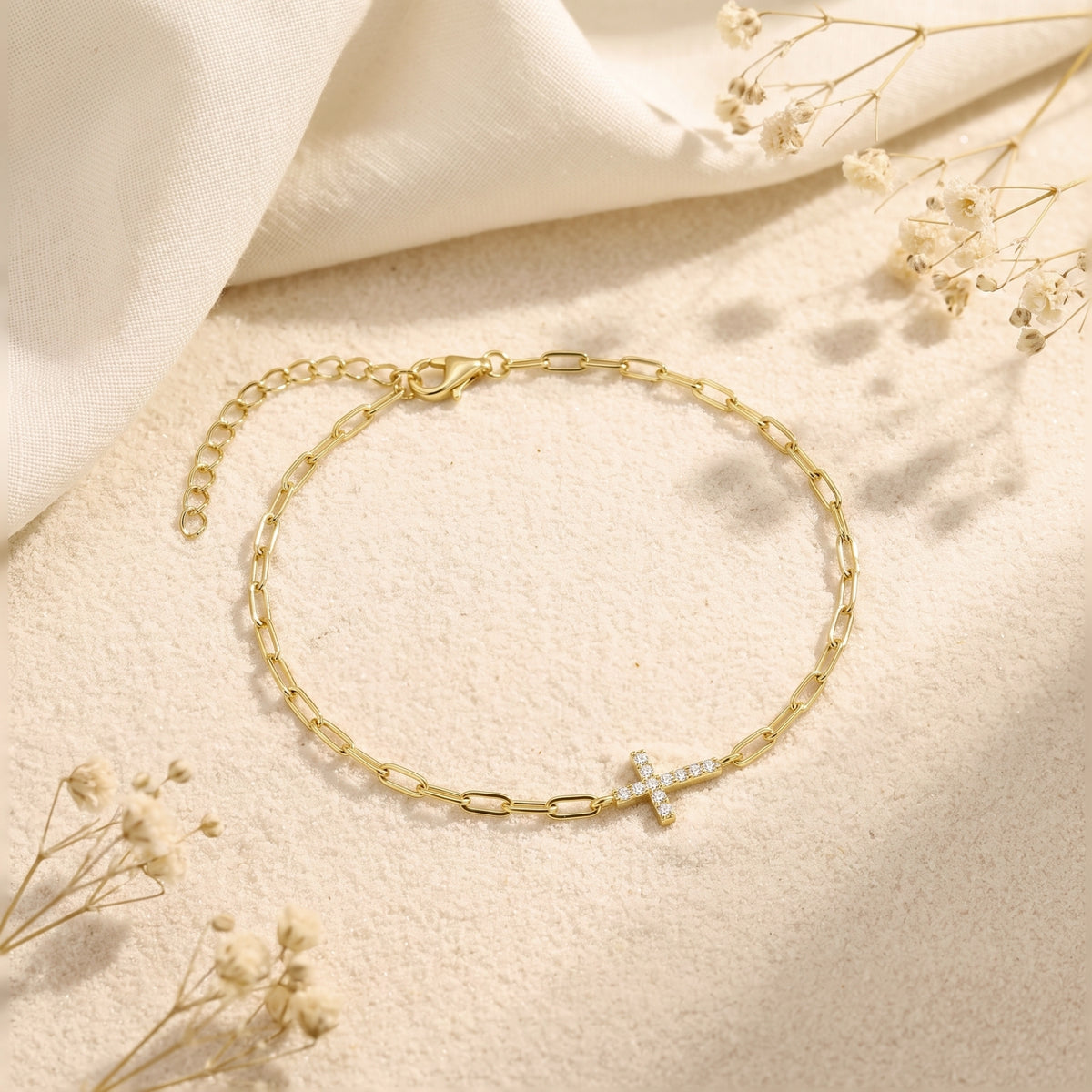 Flat-lay gold-tone paperclip bracelet showing its pave-set cross, lobster clasp, and extender chain.