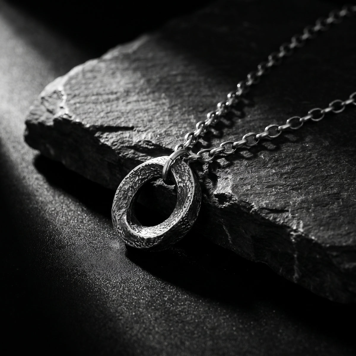 Angled close-up of the textured silver circle pendant and chain resting on a dark slate surface.
