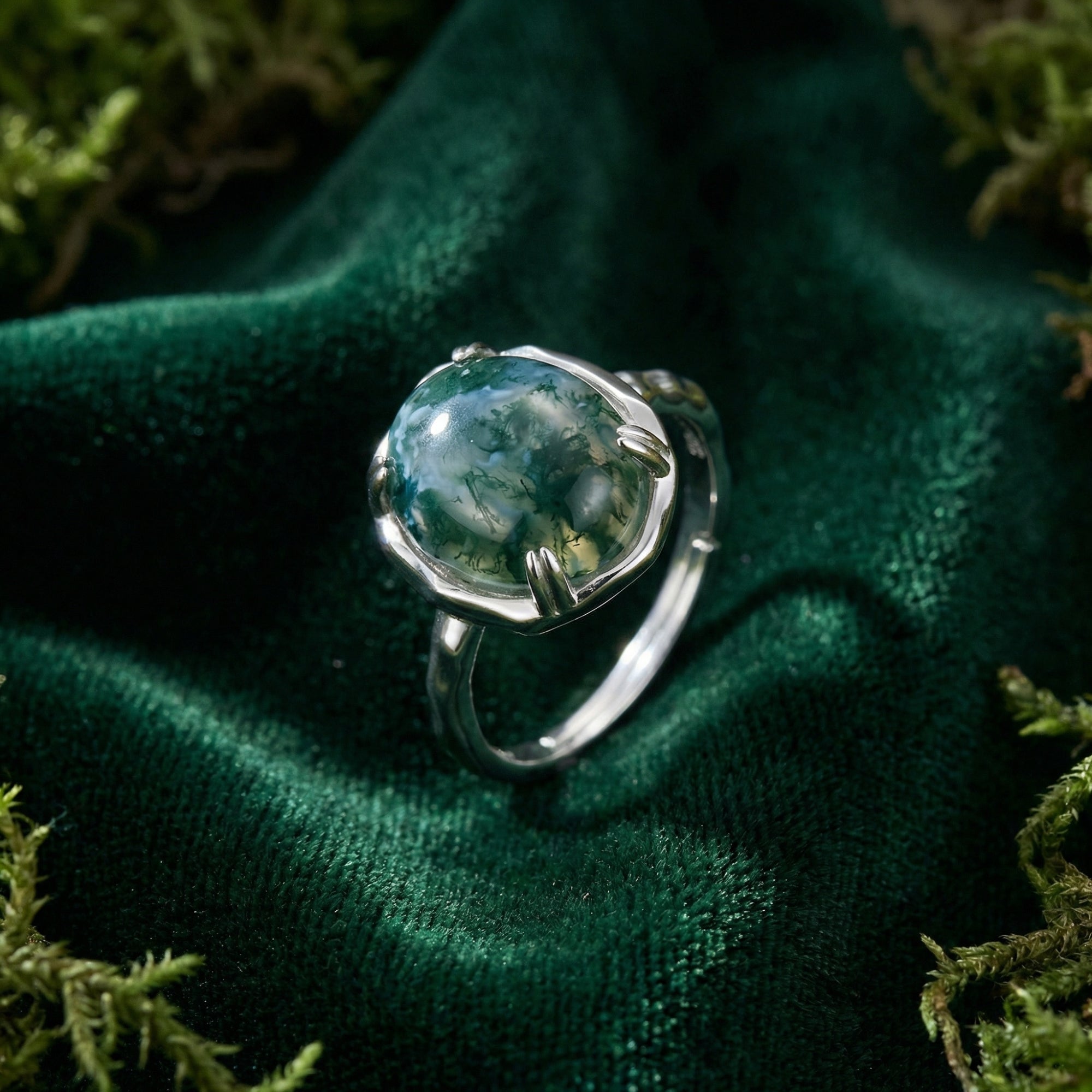 Close-up view of the sterling silver organic flow ring featuring a natural moss agate stone on green velvet.