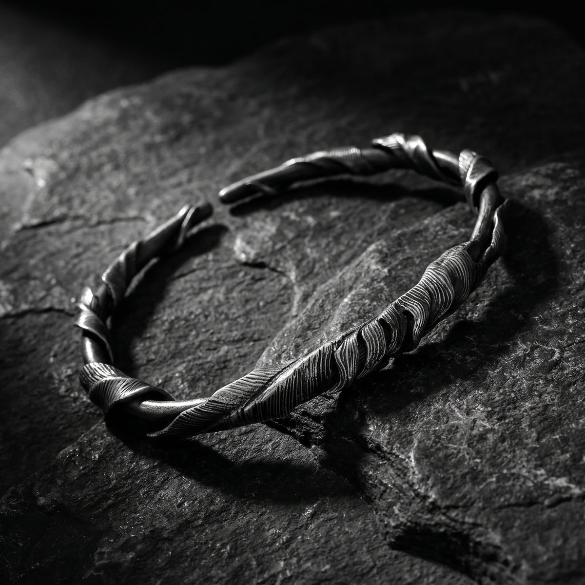 Angled view of the silver feathered twist open cuff bracelet resting on dark slate stone.