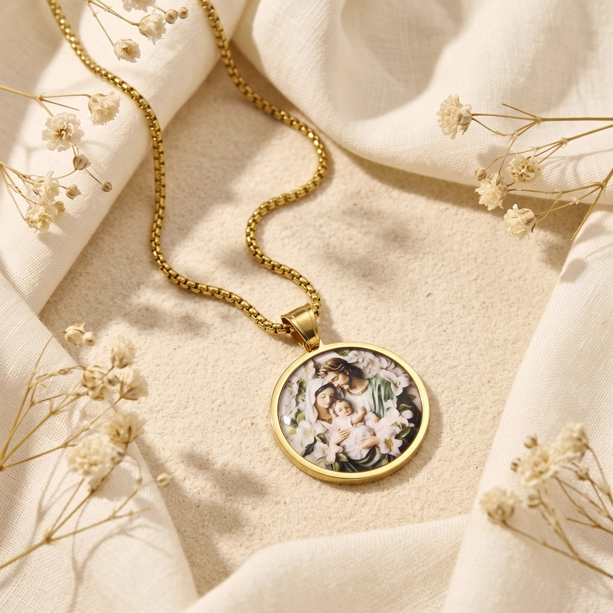 Angled flat lay of the gold-tone circular Holy Family medallion necklace on cream fabric.