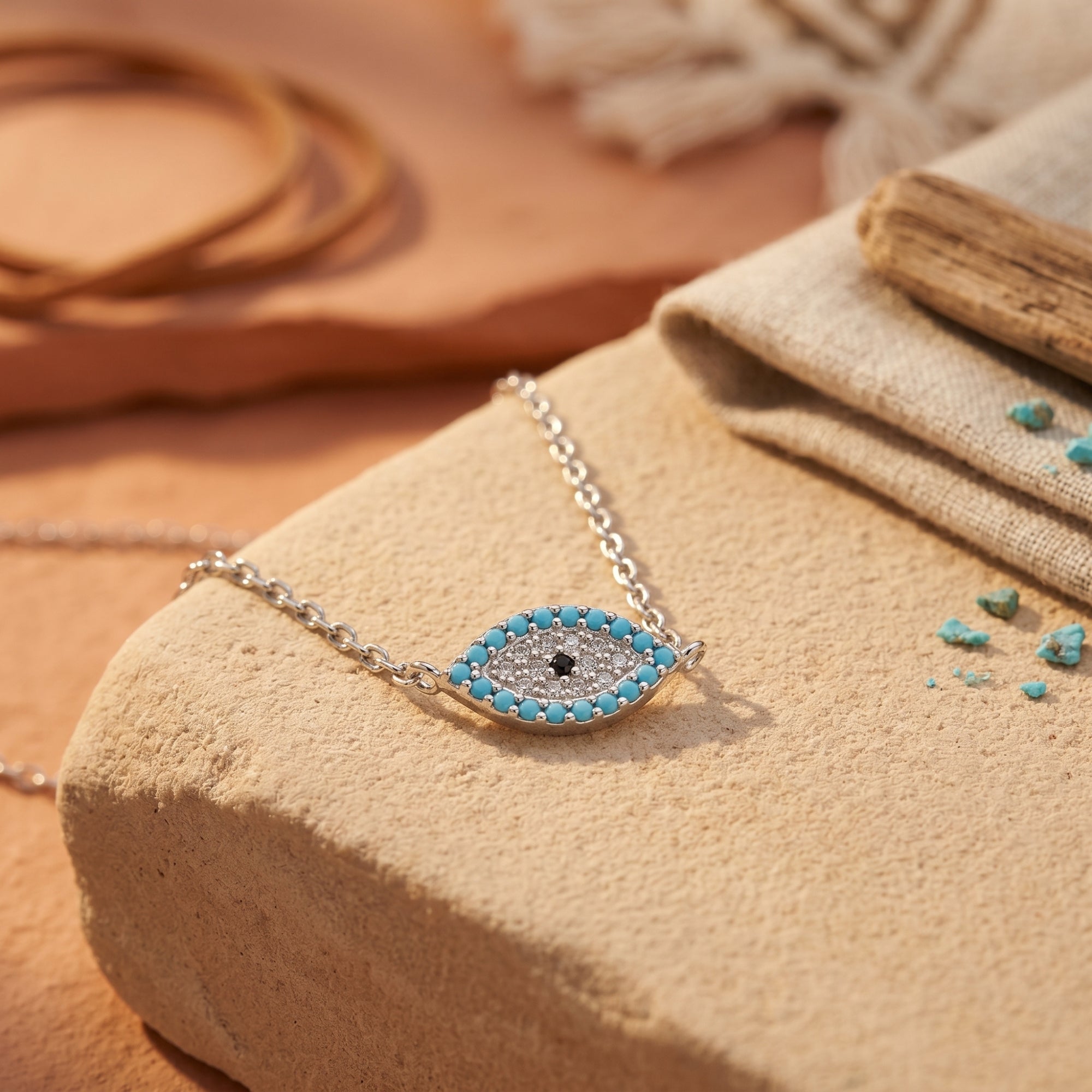Close-up of the silver eye pendant featuring 2mm turquoise cabochons and a shimmering pavé center on a stone surface.