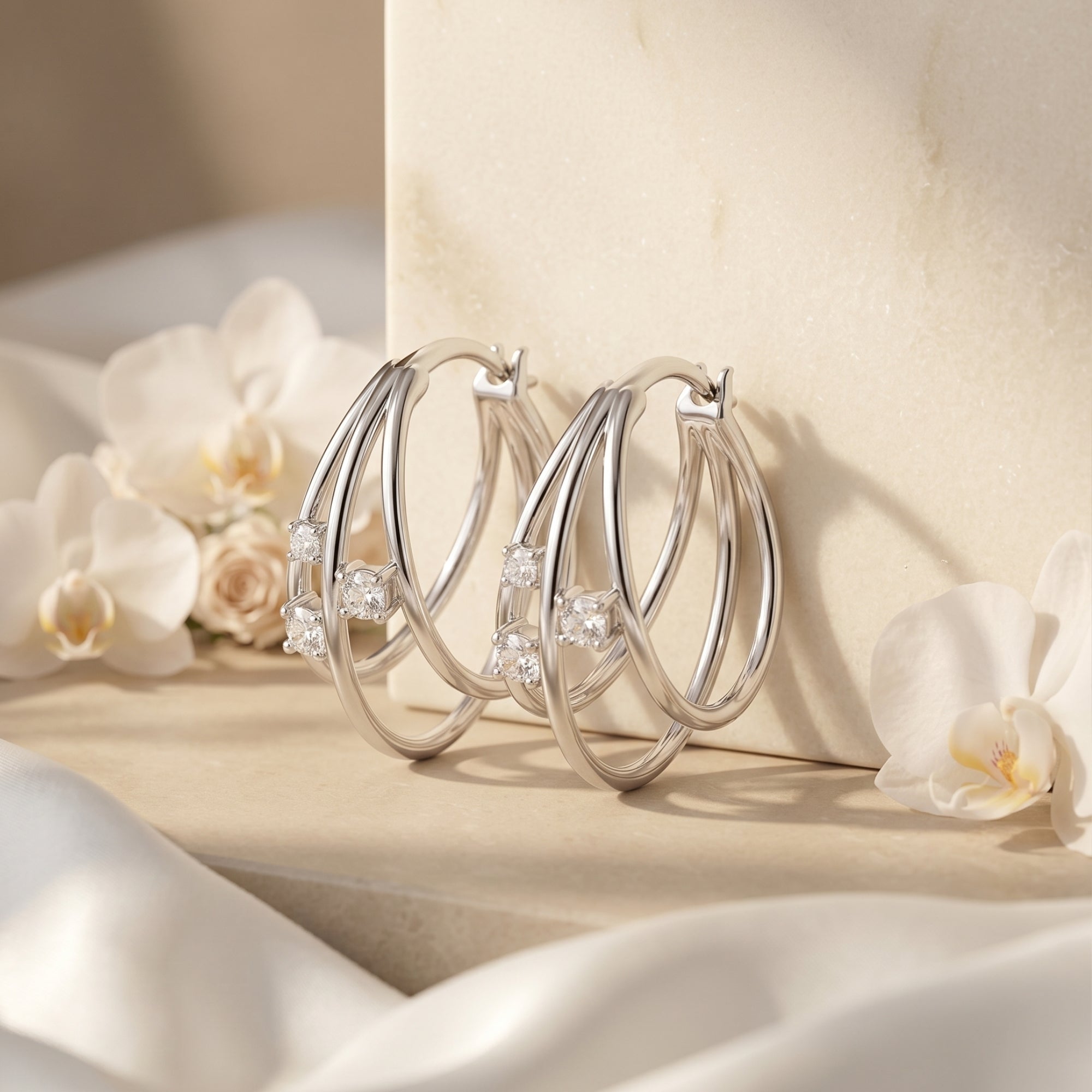 Silver triple hoop moissanite earrings displayed with white flowers and silk.