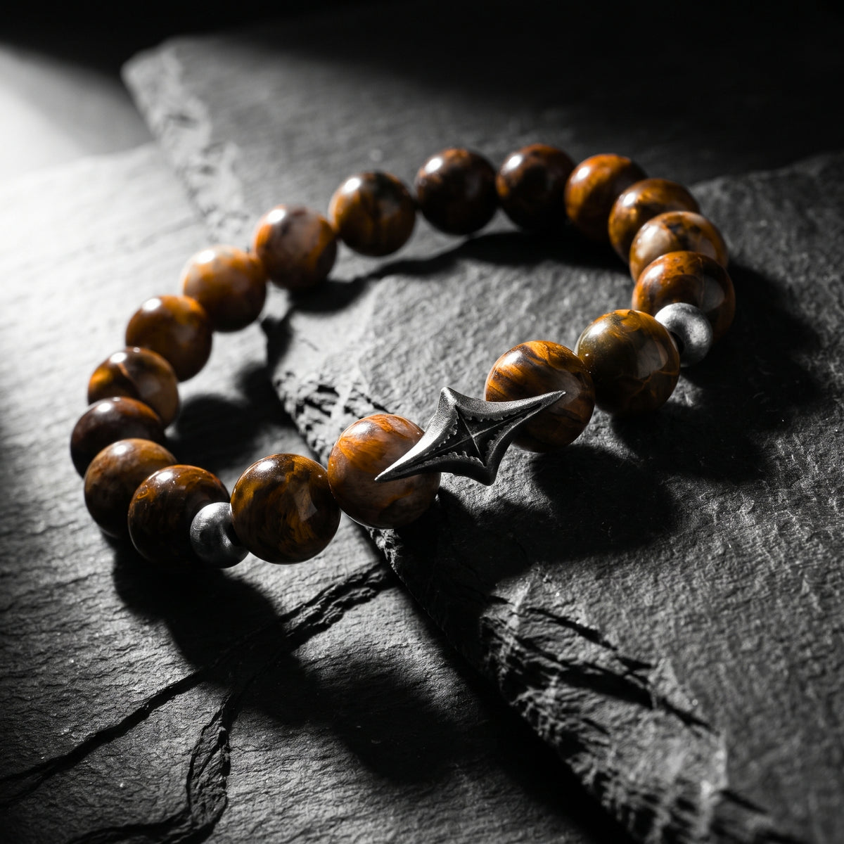 Angled view of the North Star beaded bracelet with brown gemstone beads and an oxidized silver star station on slate