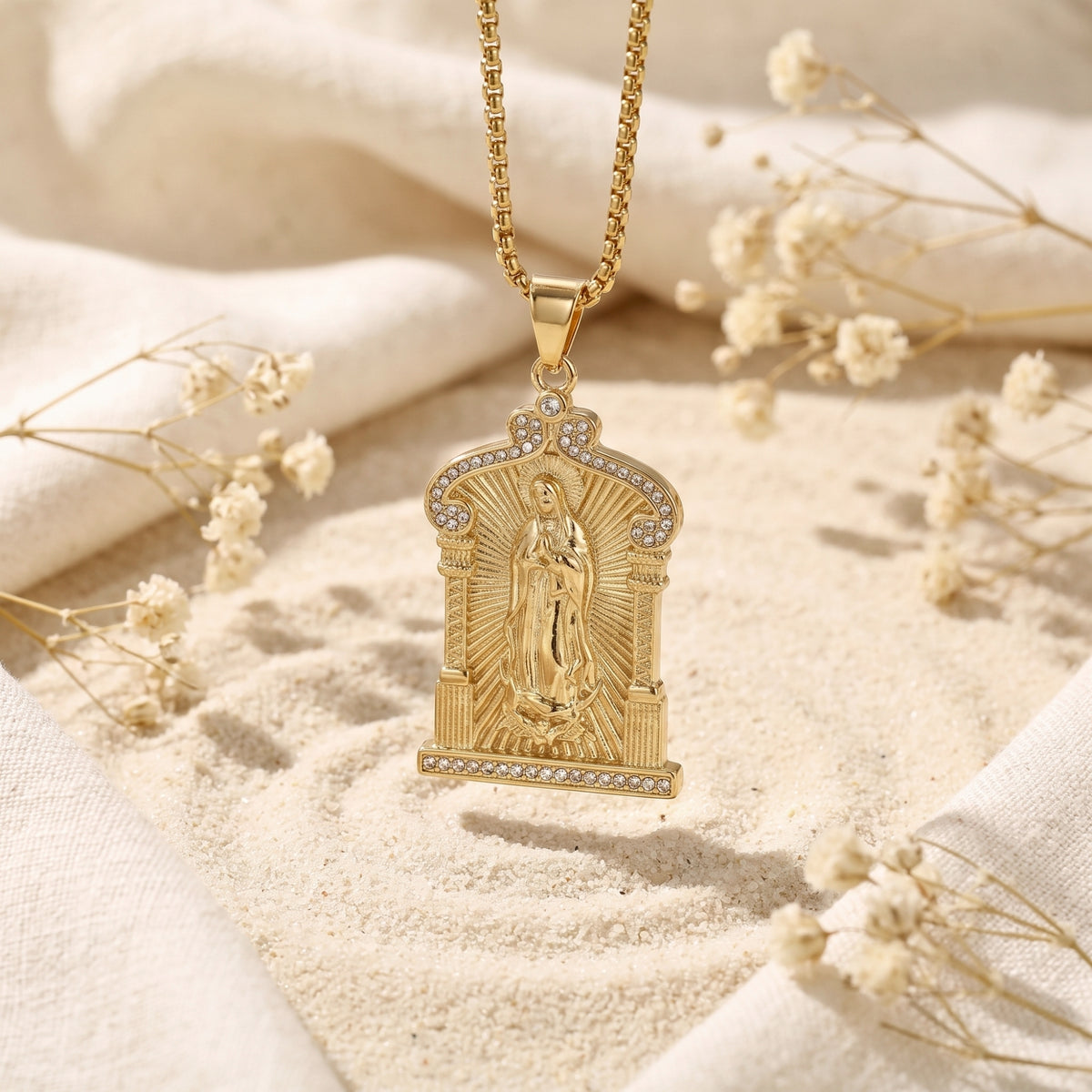 Gold-tone Guadalupe arch pendant hanging over sand, with a Virgin Mary relief and crystal-lined frame.
