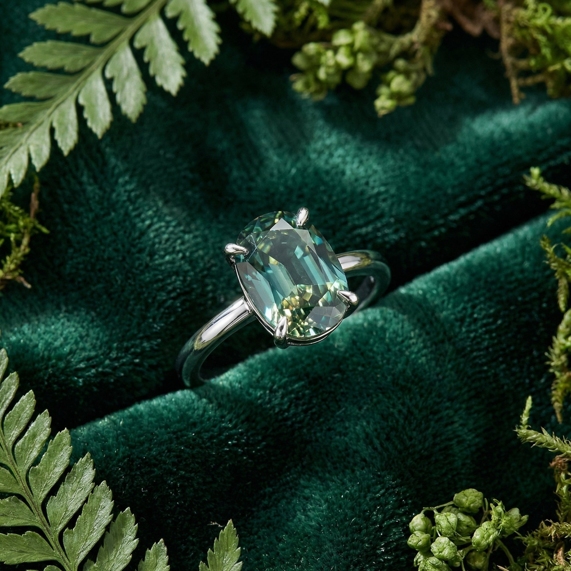 Close-up of a 2CT oval cut green moissanite ring in a silver claw setting on a green velvet background.