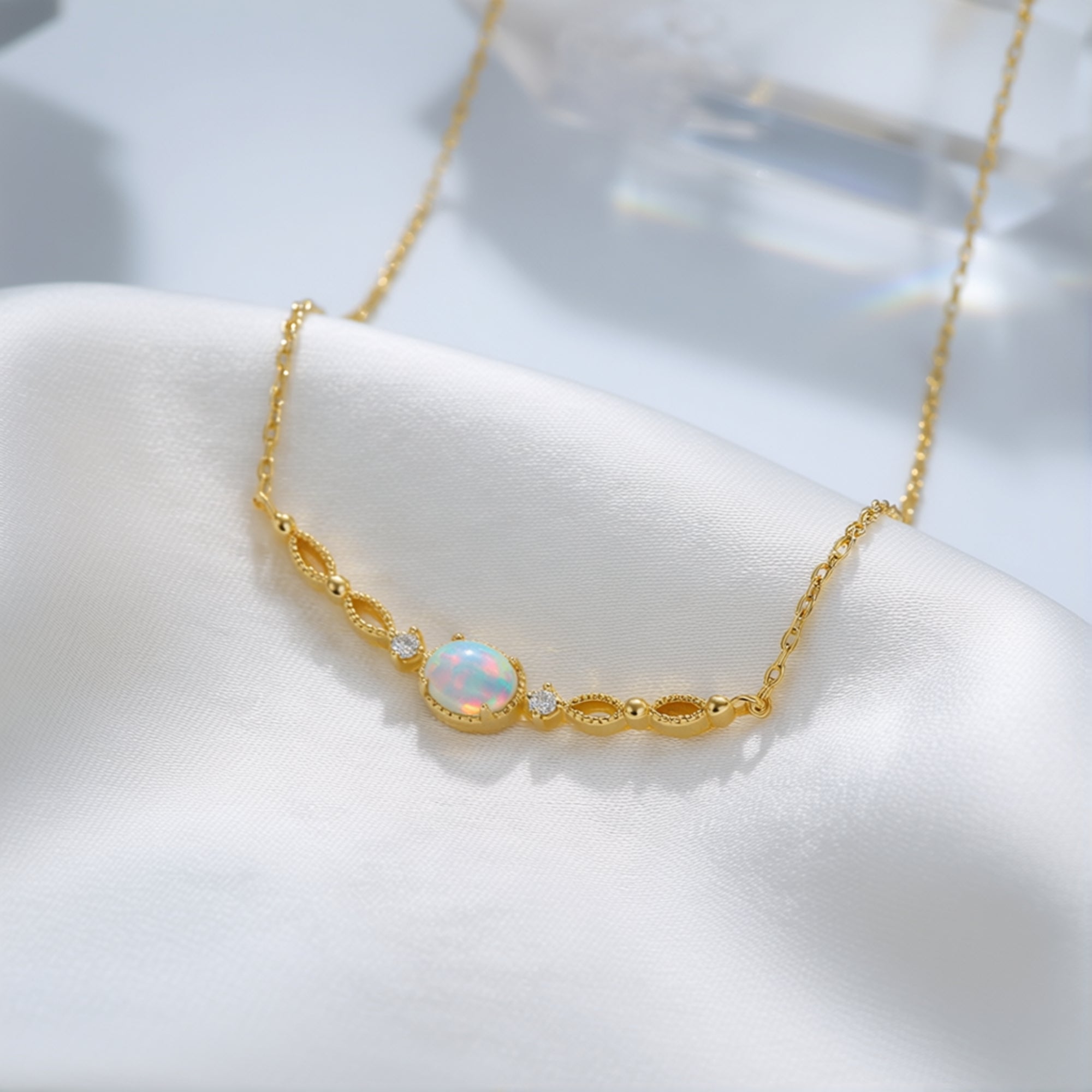 Close-up of an oval white opal pendant in a gold-tone sterling silver filigree setting on white silk.