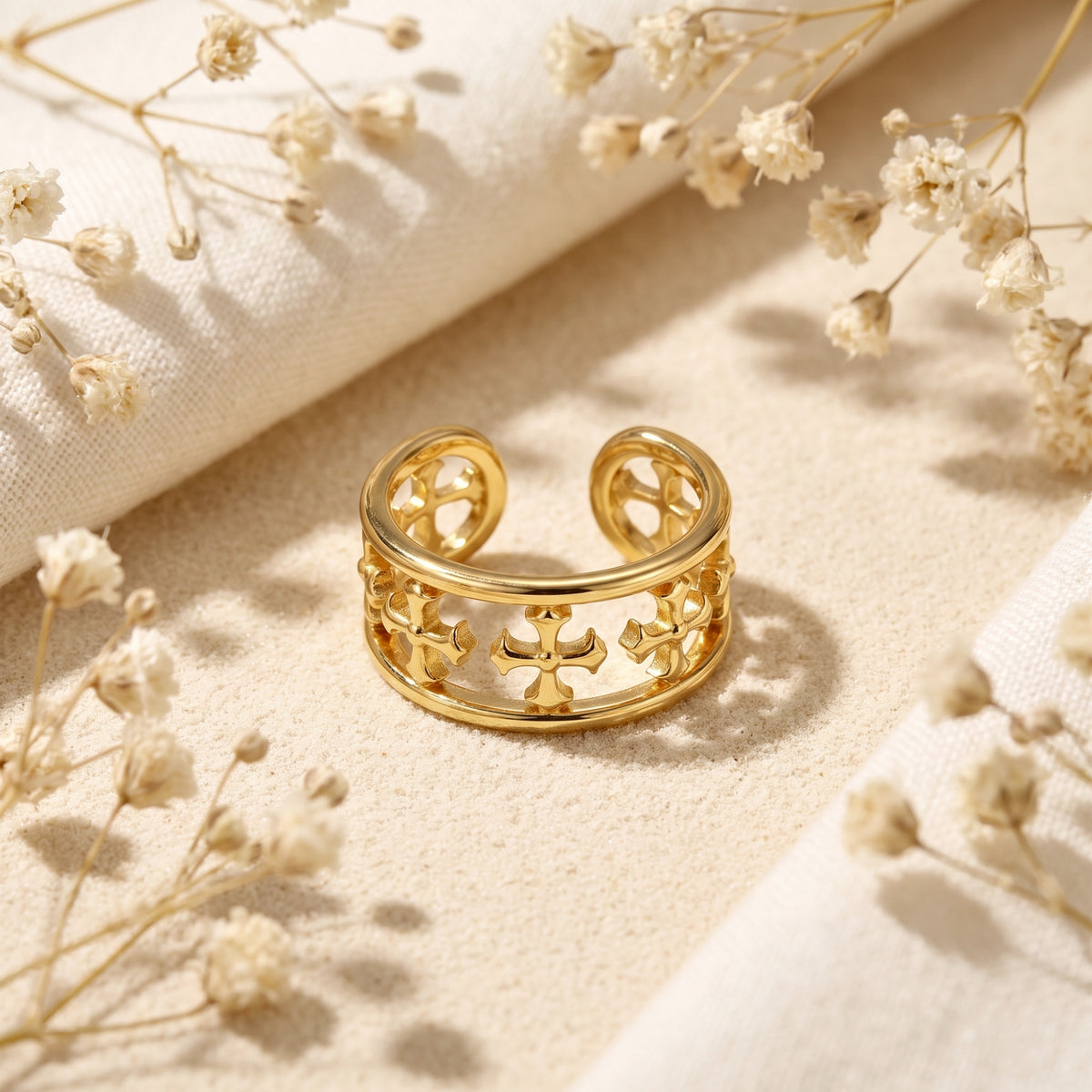 Front-facing view showing the open back and cross motifs of the gold cuff ring on sand.