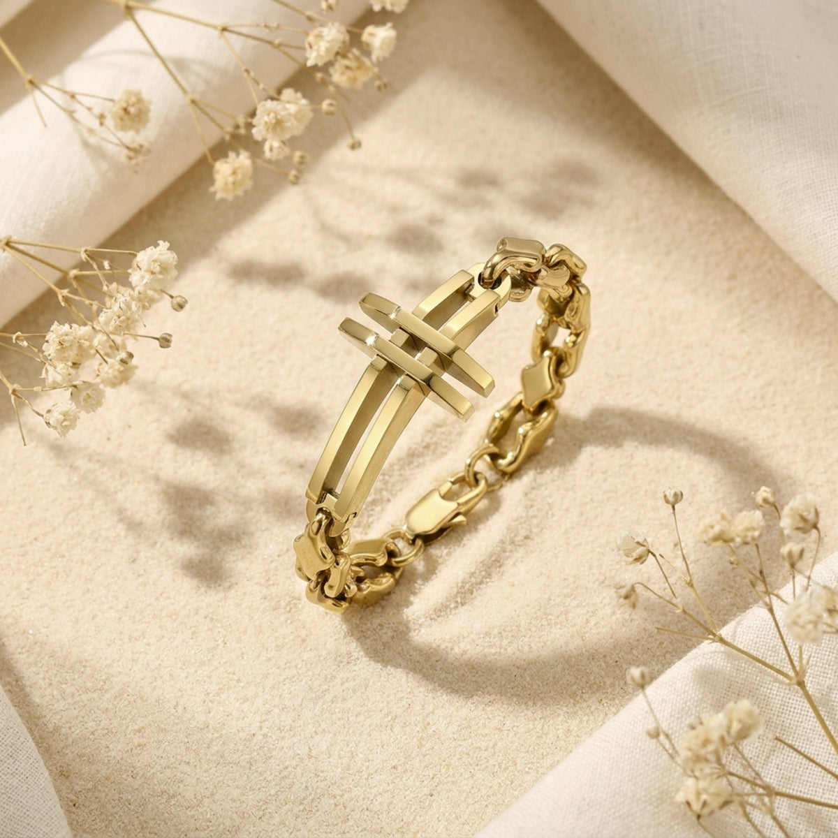 Angled view of the gold-tone cross link bracelet on sand, highlighting its raised cross centerpiece.