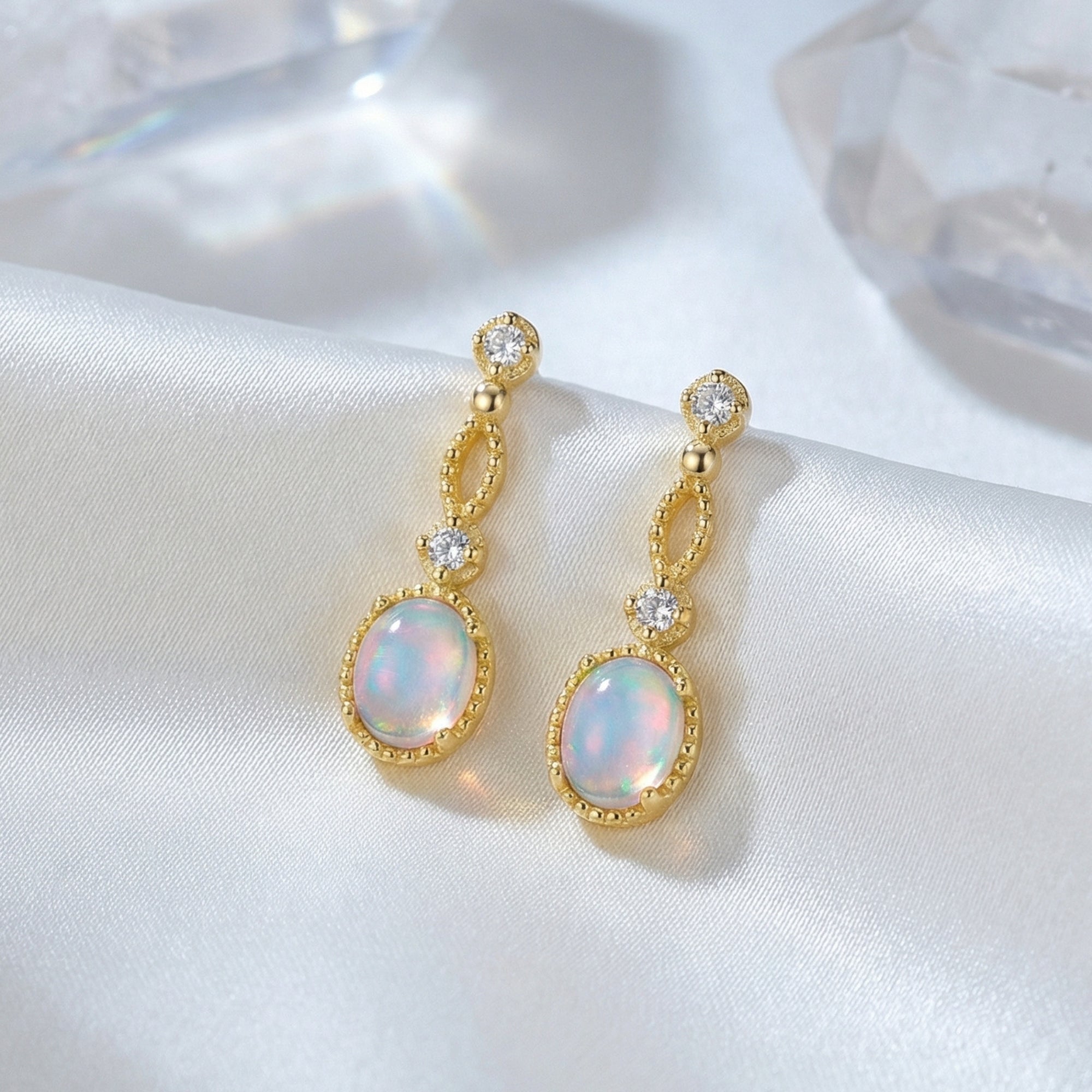 Macro view of gold-tone Lorelei earrings showing the play-of-color in the oval white opals on white silk.