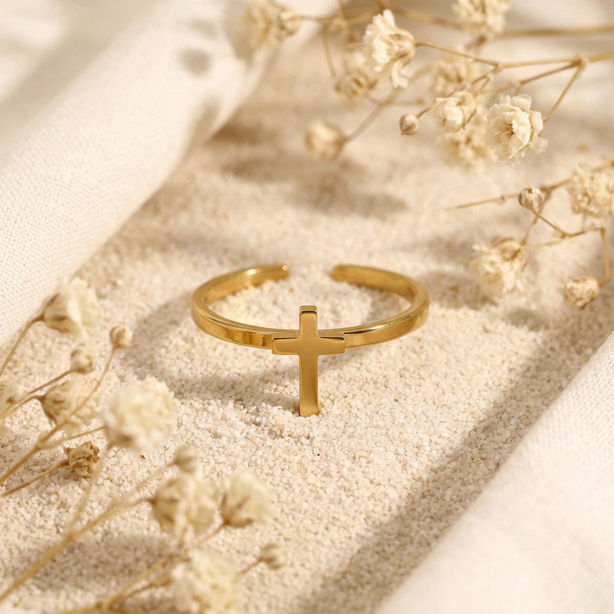 Upright view of the gold-tone cross ring showing the small cross centerpiece on fine sand.