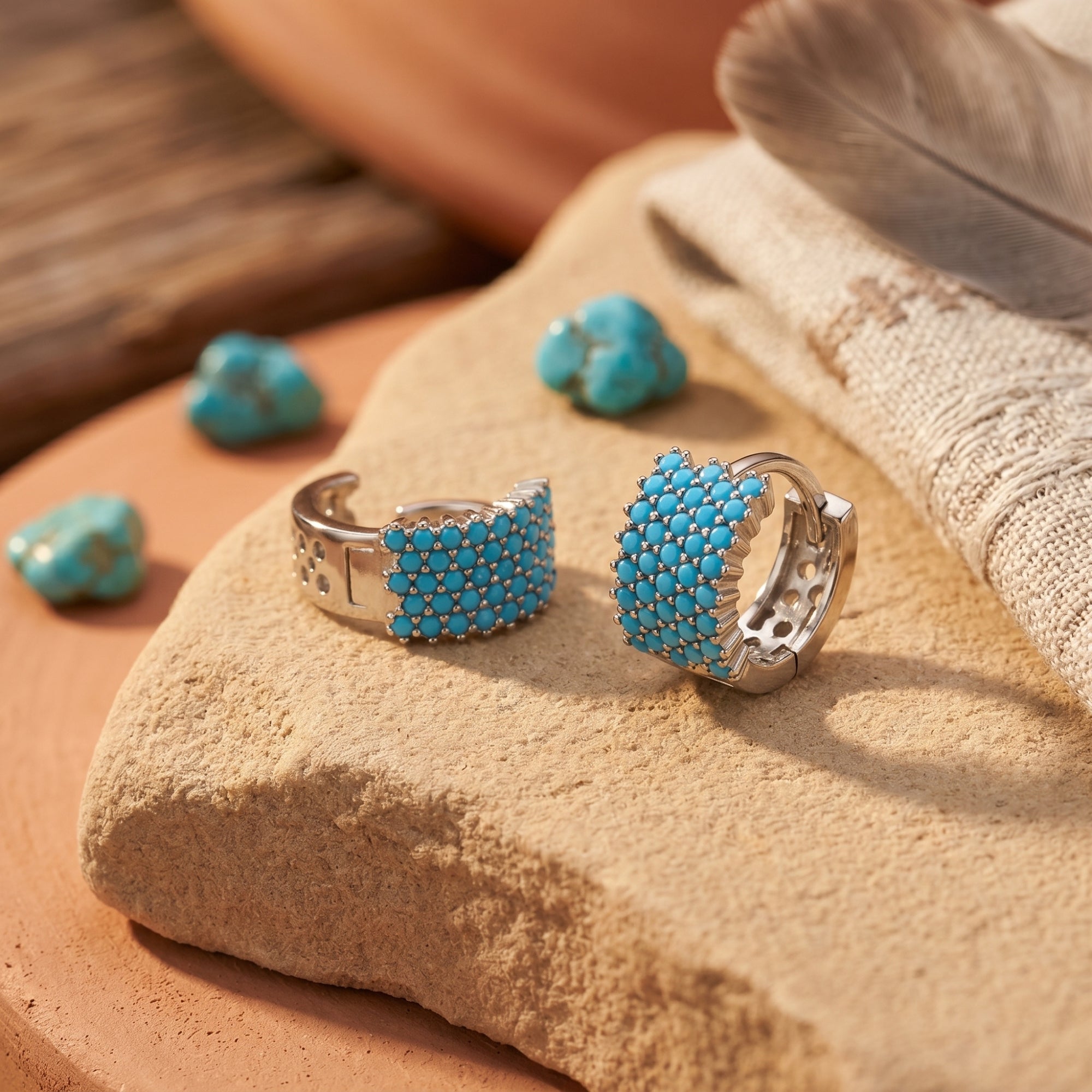 Two silver turquoise huggie earrings on a desert stone, showing the cabochon cluster and side profile.